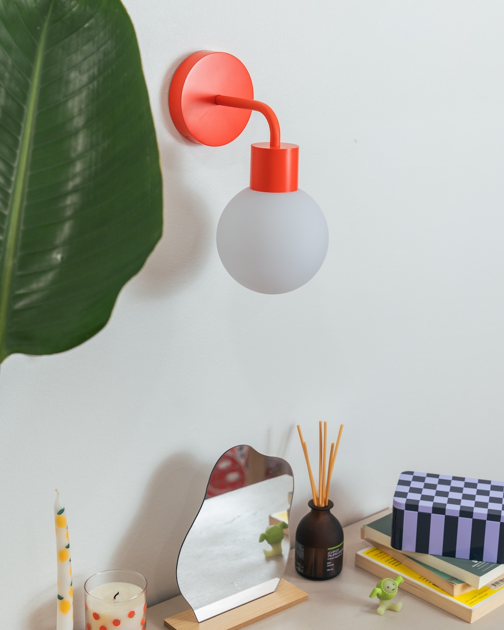 Orange wall light above a desk with a mirror and decorative items.