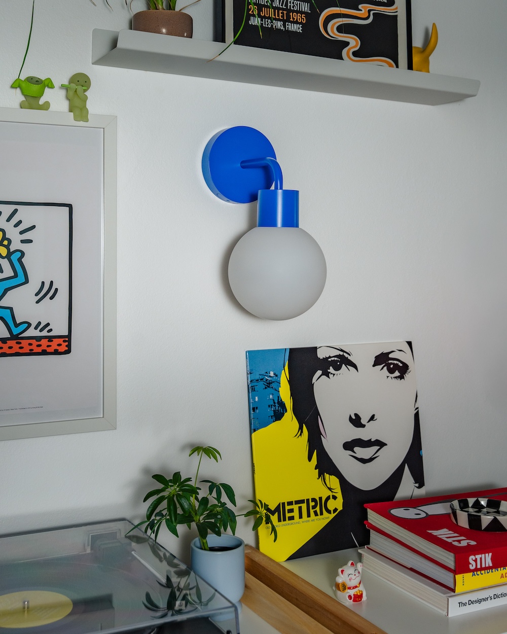 Interior with wall art, a blue wall light, books, a plant, and a vinyl record display.