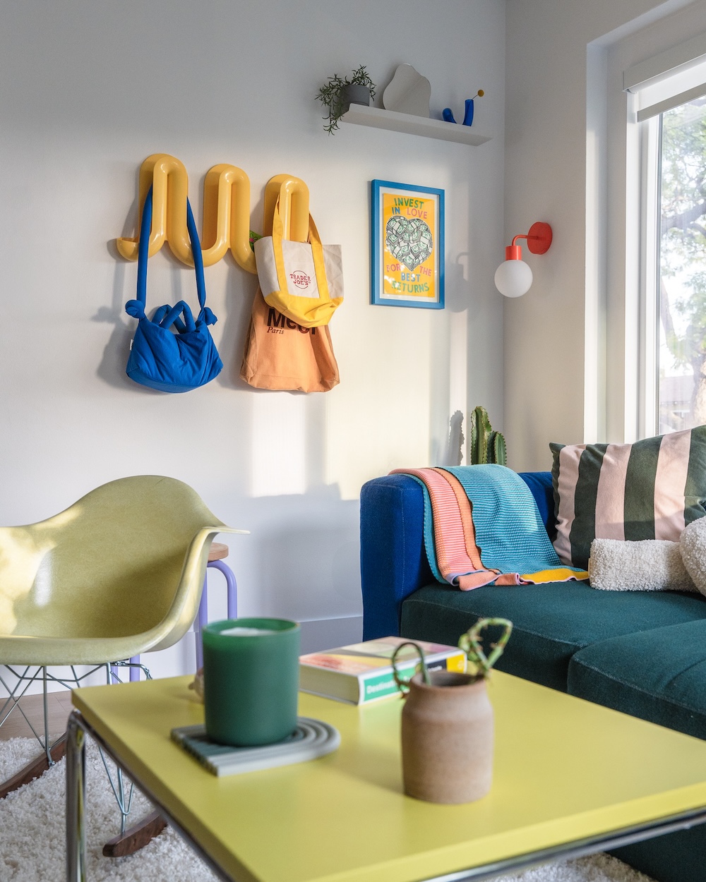 Colorful living room with wall hooks, bags, artwork, and a blue couch.