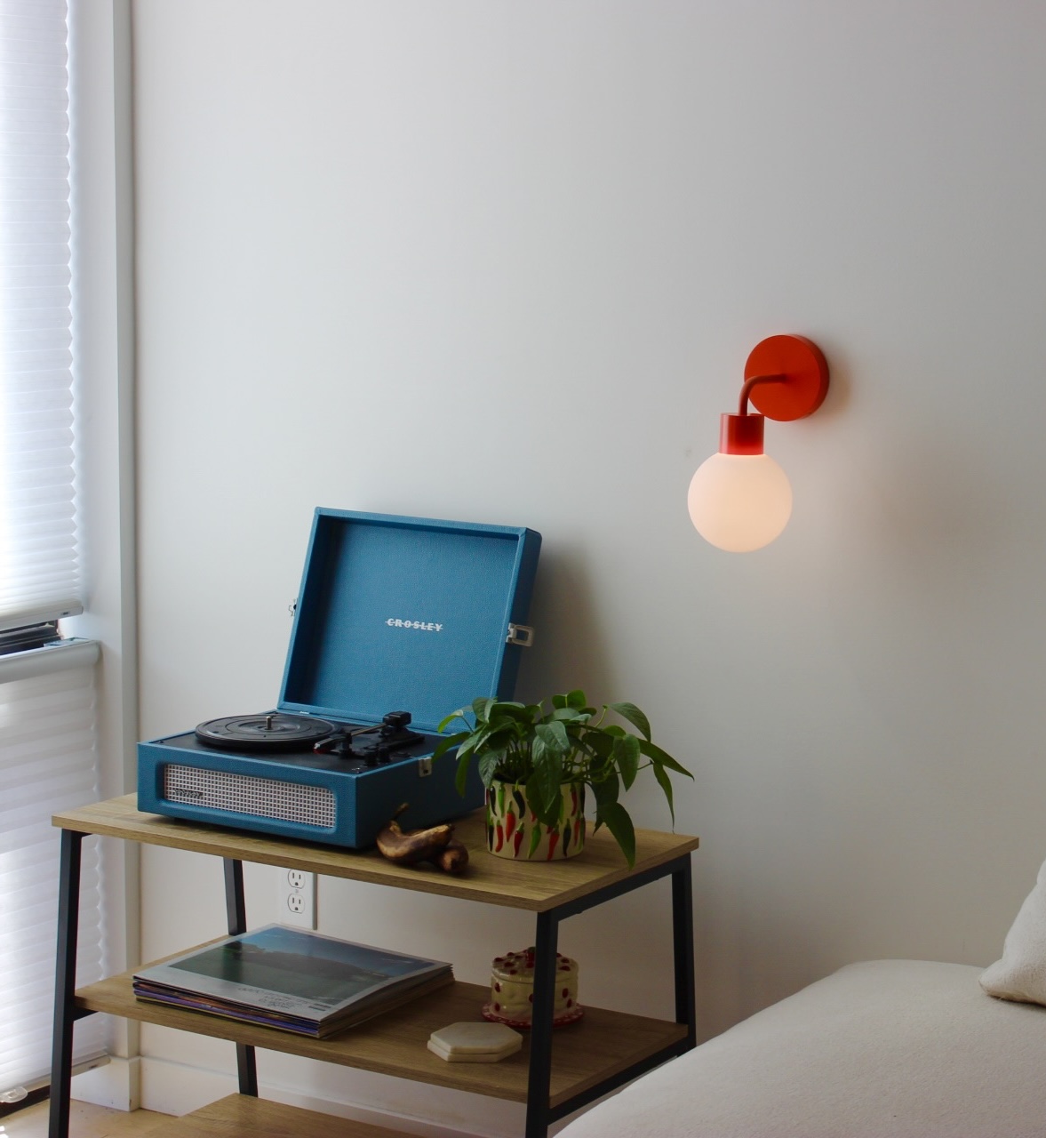 Blue record player on a shelf with a plant, next to a wall lamp.