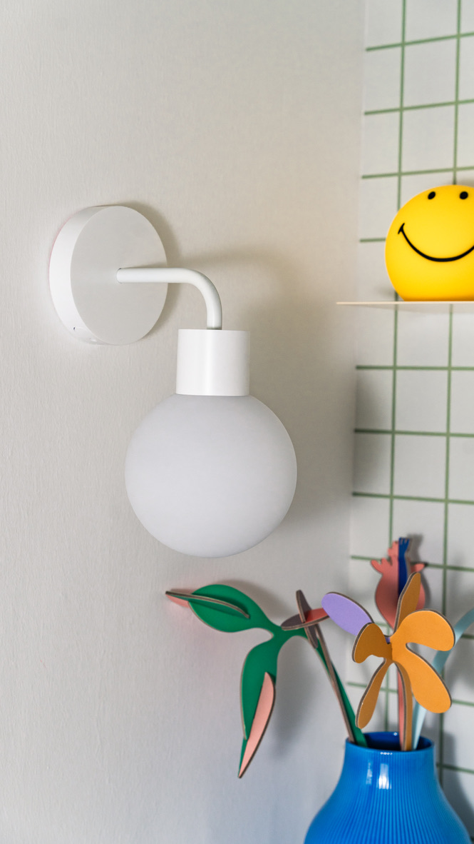 White wall lamp, smiley face lamp, colorful plant decor in blue vase.