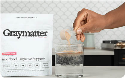 Person adding powder to a glass of water next to Graymatter packet.