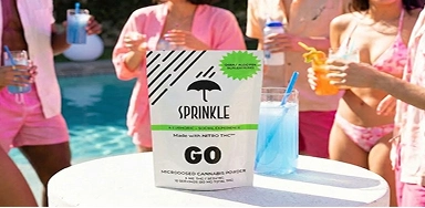 A pouch of Sprinkle GO cannabis powder on a table next to a blue drink at a pool party.