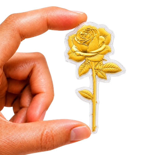 A hand holds a small, gold, rose-shaped collectible encased in plastic against a white background.