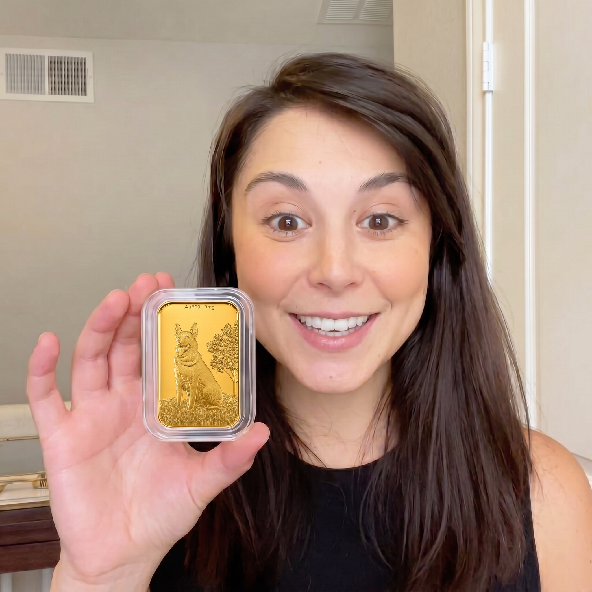A smiling woman holds up a small, encased gold bar with an engraved dog on it.