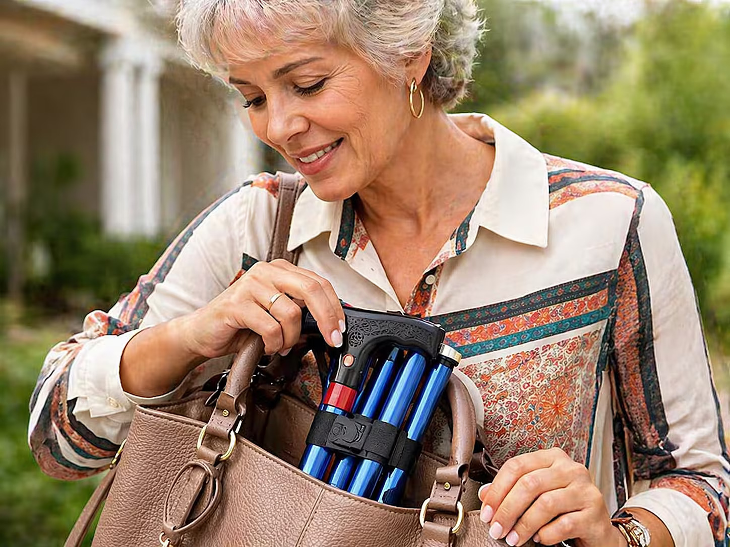 A smiling woman places a folded blue walking cane into her brown handbag.