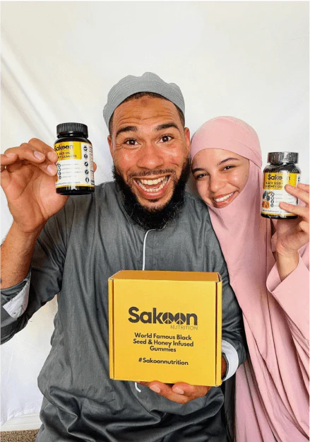 Two people smiling, holding supplement bottles and a yellow box with 'Sakoon Nutrition' branding.