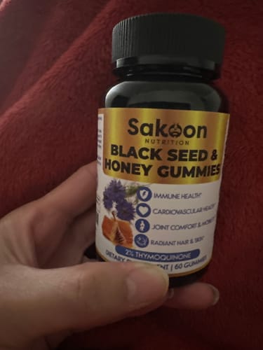 Hand holding a bottle of black seed and honey gummies.