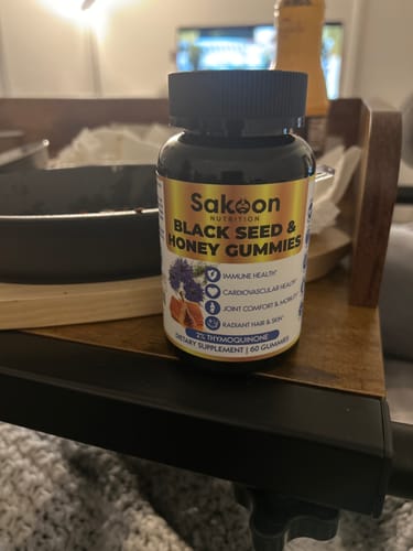 A bottle of black seed and honey gummies on a wooden table.