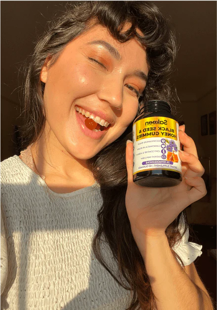 Person smiling, holding a bottle of black seed honey gummies.