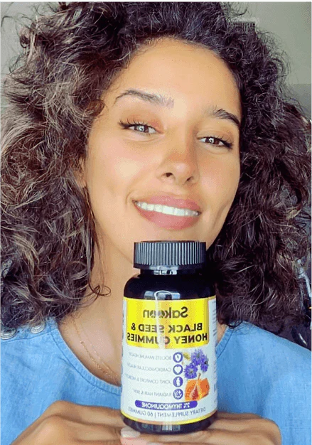 Person smiling and holding a bottle of black seed and honey gummies.