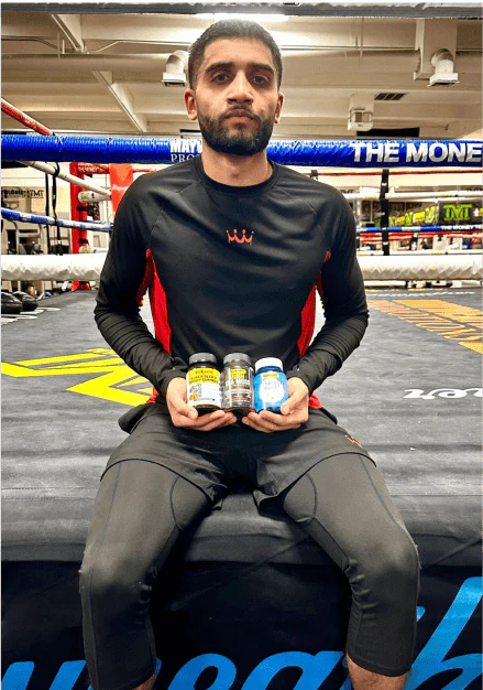 Person sitting in a boxing ring holding three supplement bottles.