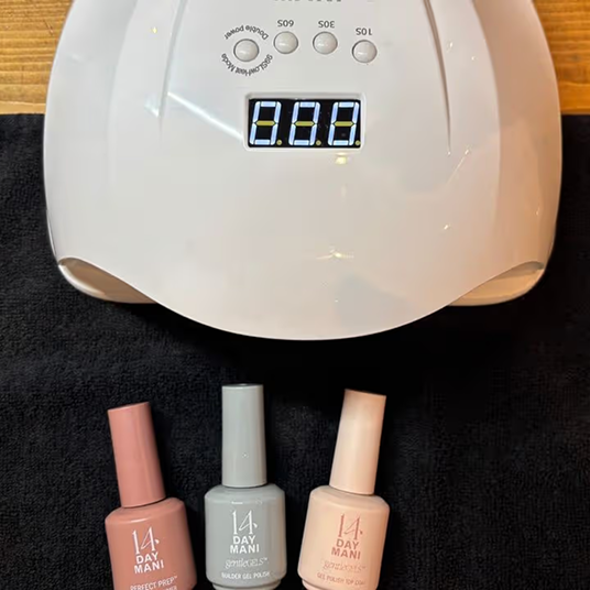 Three bottles of 14 Day Mani gel nail polish sit in front of a white UV nail lamp.