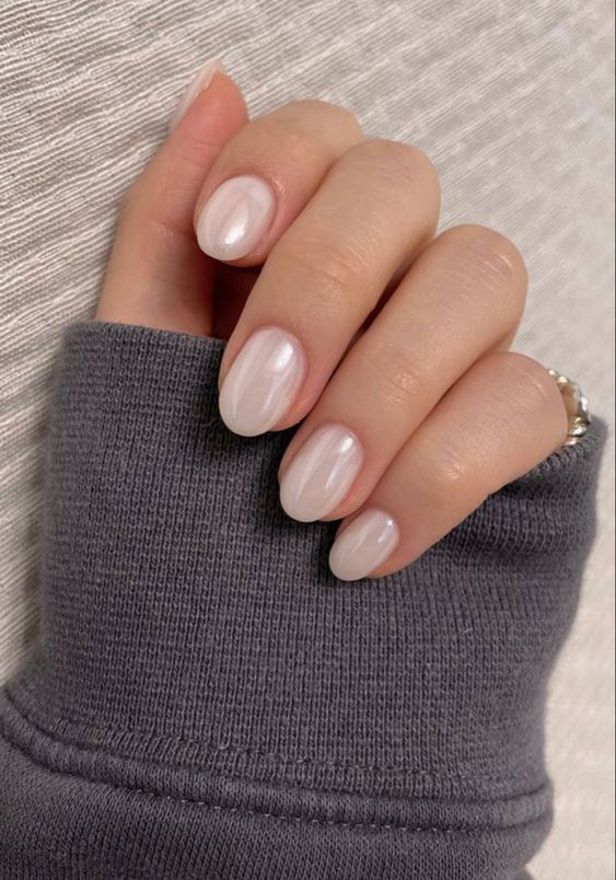 Close-up of hand with pearlescent nails and gray sleeve.