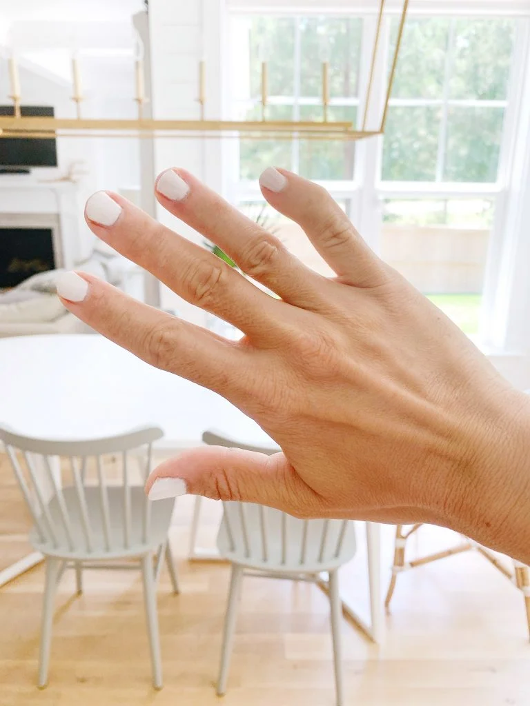 A hand with white nail polish in a modern dining room setting.