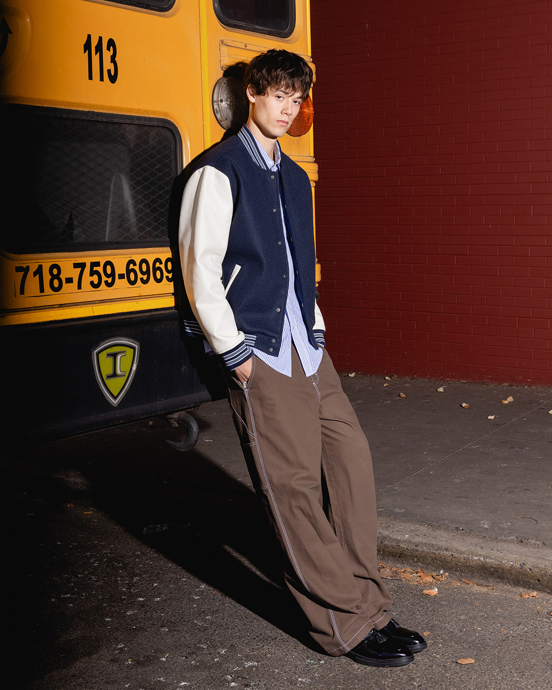 Person leaning against a yellow bus next to a red brick wall.