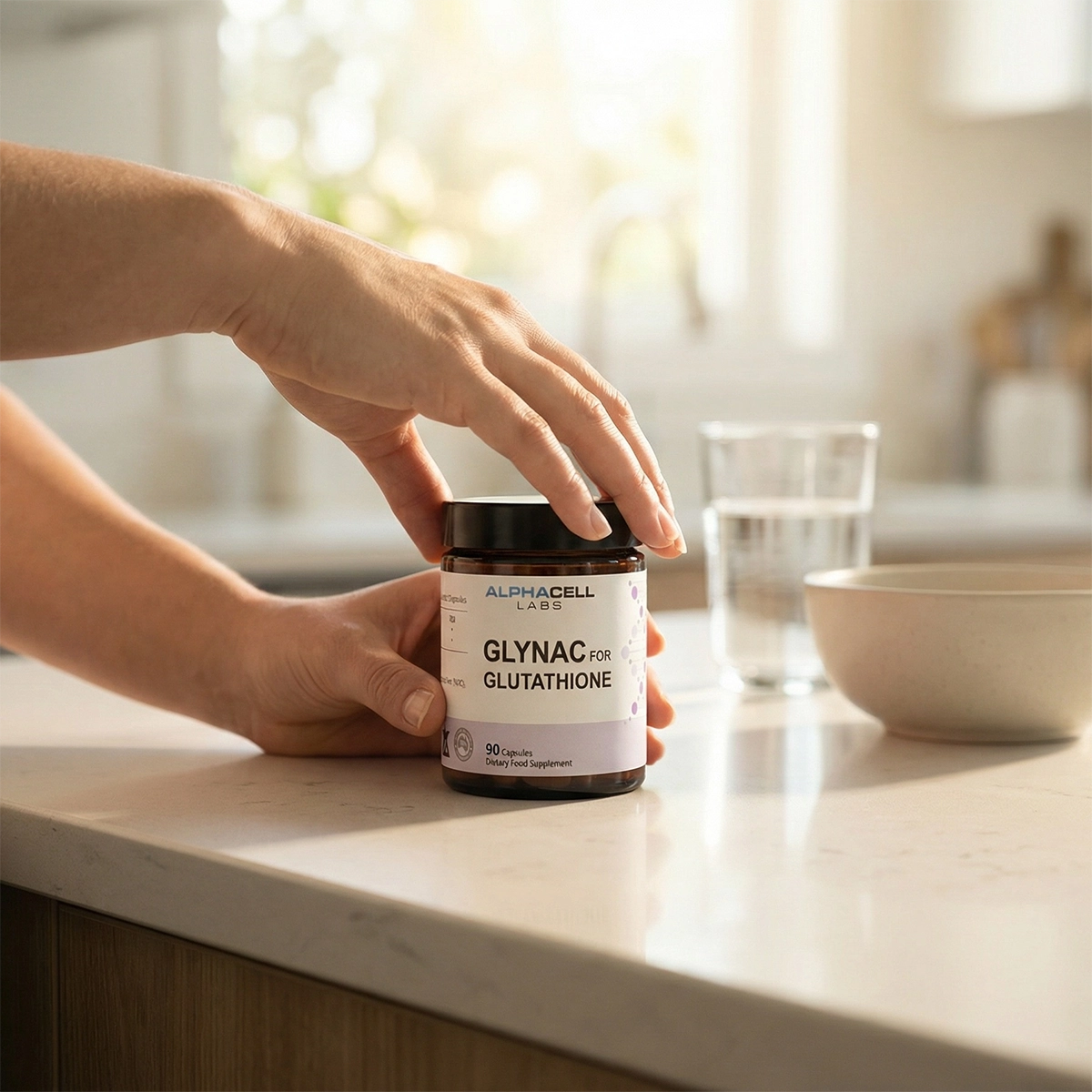 A person's hands hold a bottle of Alphacell Labs Glynac for Glutathione on a kitchen counter.