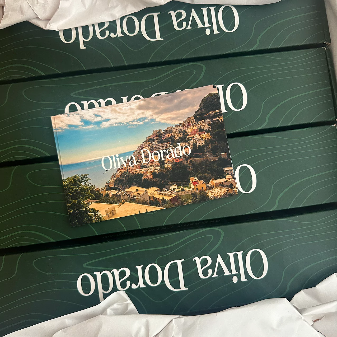 Green boxes labeled 'Oliva Dorado' with a scenic postcard on top.