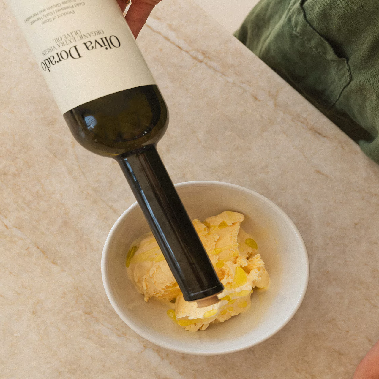 Olive oil being poured over vanilla ice cream in a bowl.