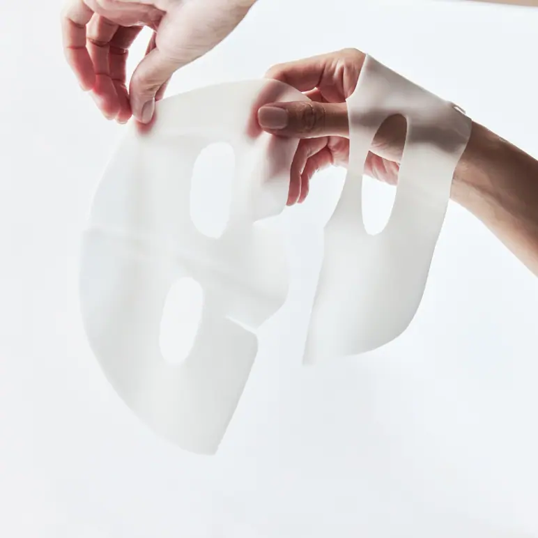 Two hands holding a translucent face mask sheet.