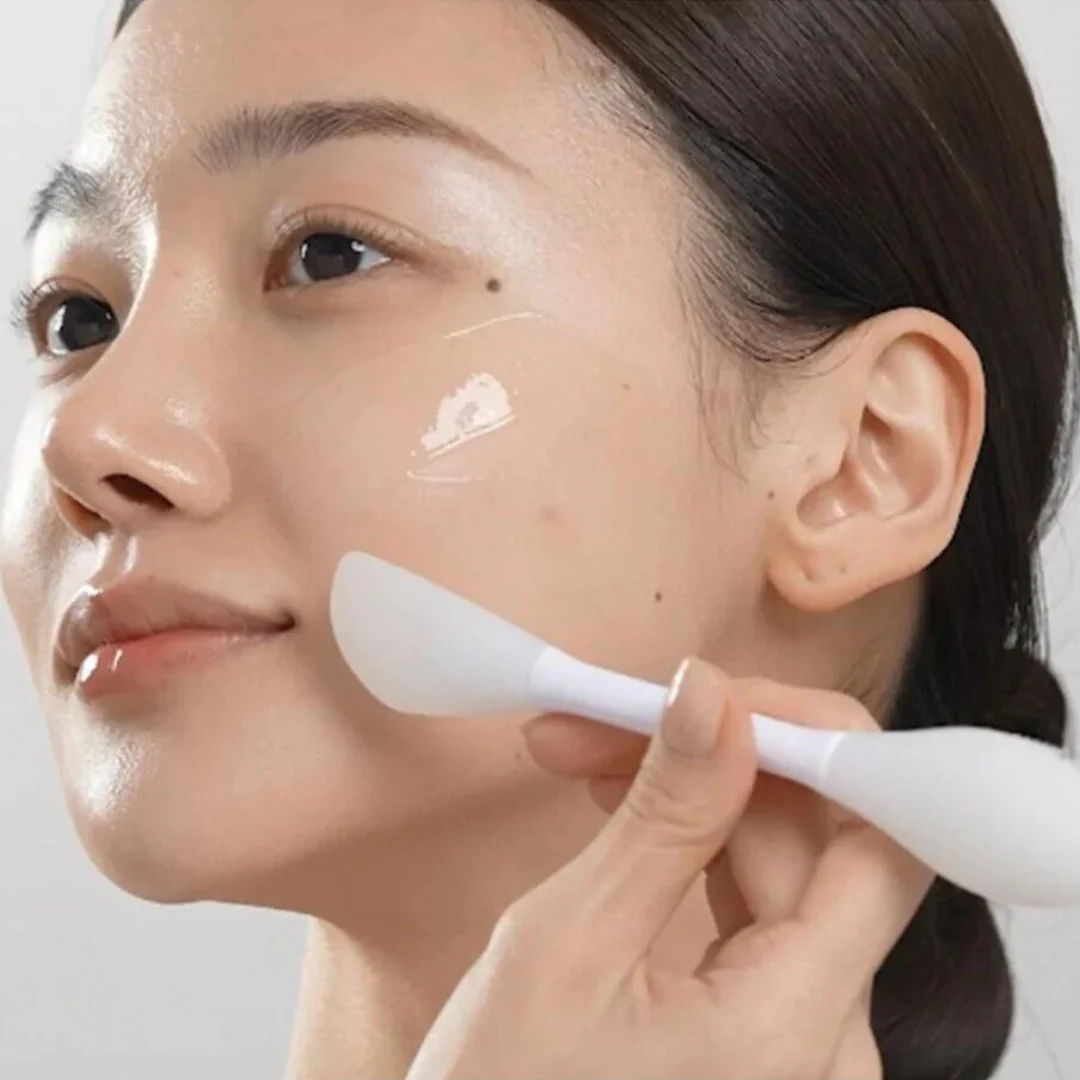 Person applying cream to face with a spatula.