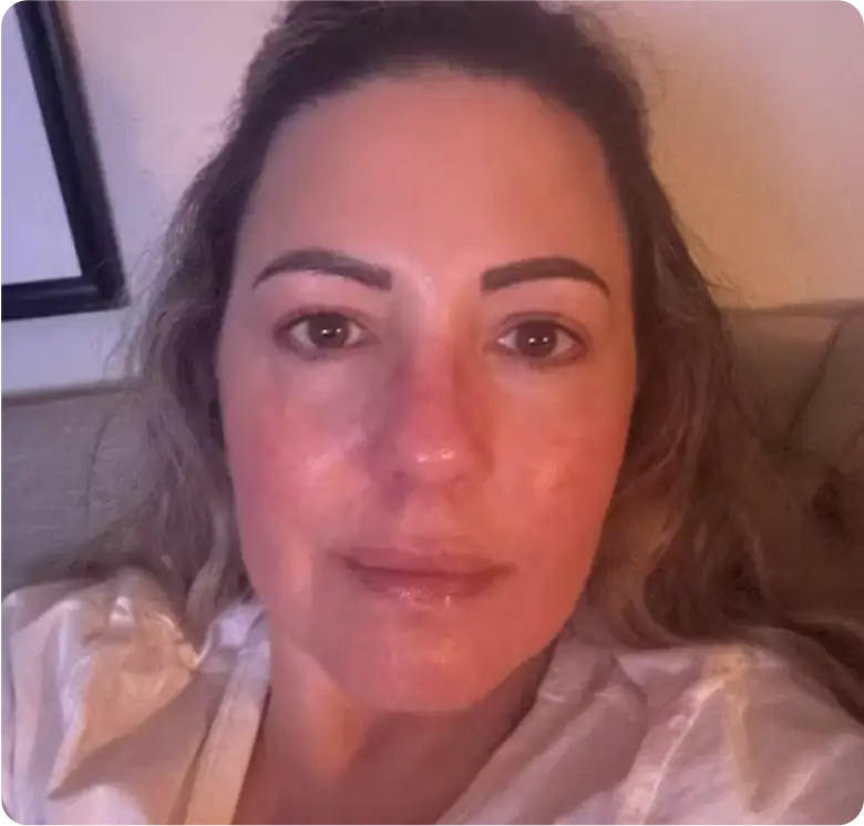 A close-up of a person with long hair indoors, wearing a white shirt.