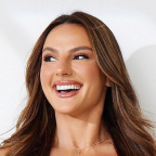 A person with long brown hair smiling against a plain background.