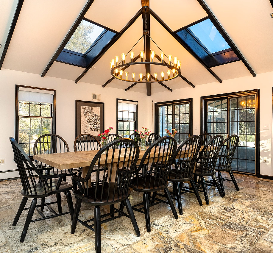 A dining room with a long wooden table, black chairs, and a large chandelier under a vaulted ceiling.