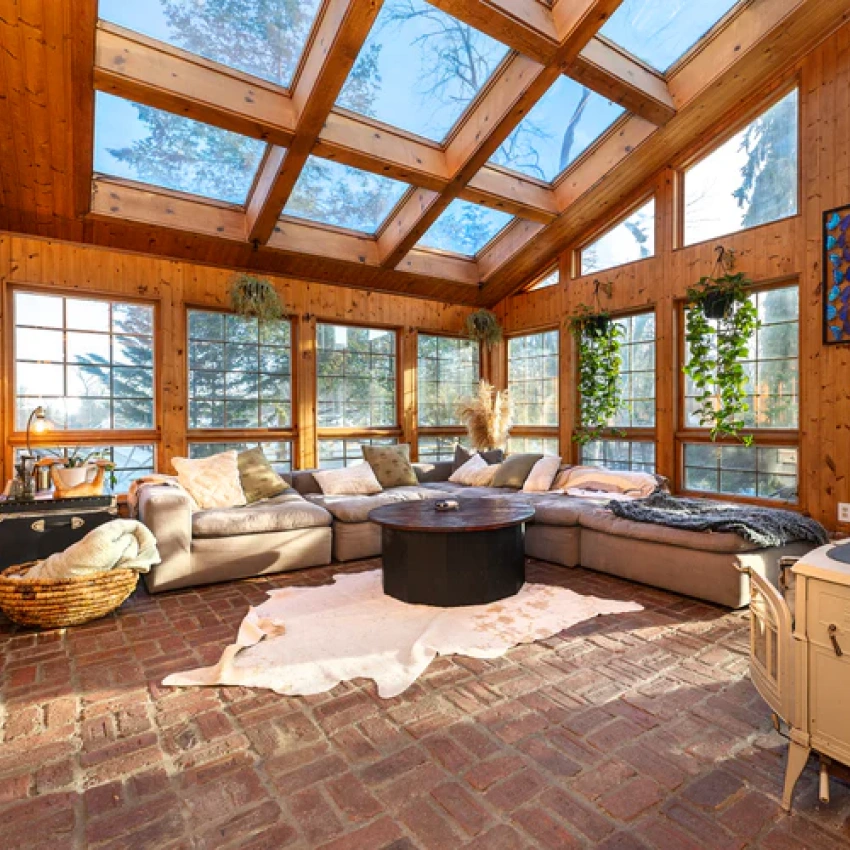 A sun-filled room with a glass ceiling, wood-paneled walls, brick floors, and a large sectional sofa.