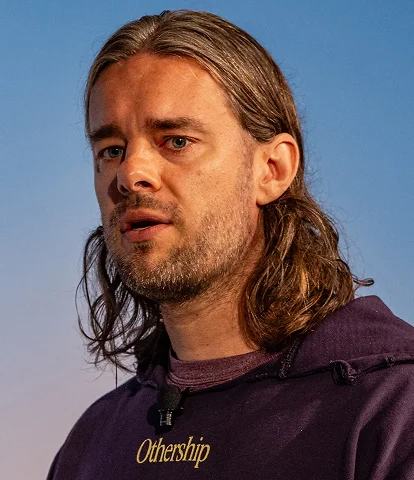 Person with long hair wearing a purple hoodie, set against a plain blue background.