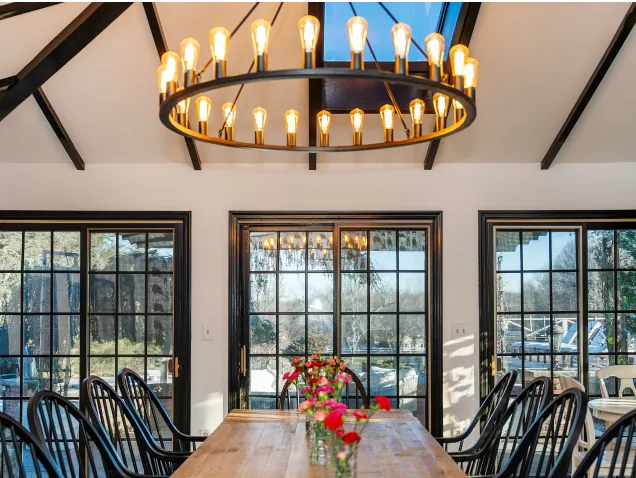 Dining room with wooden table, chairs, chandelier, and large windows.