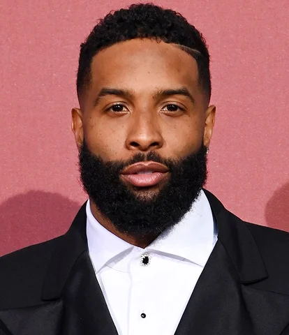 Man with a beard in a formal suit against a red background.