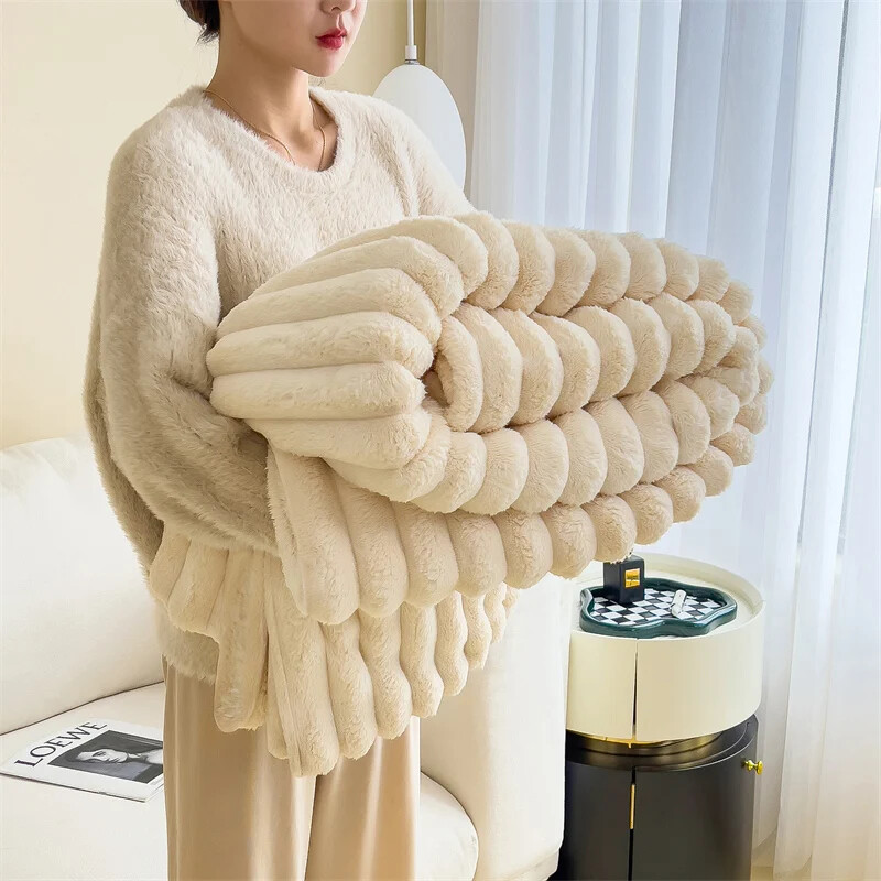 Person holding a large, fluffy, beige blanket in a cozy room.