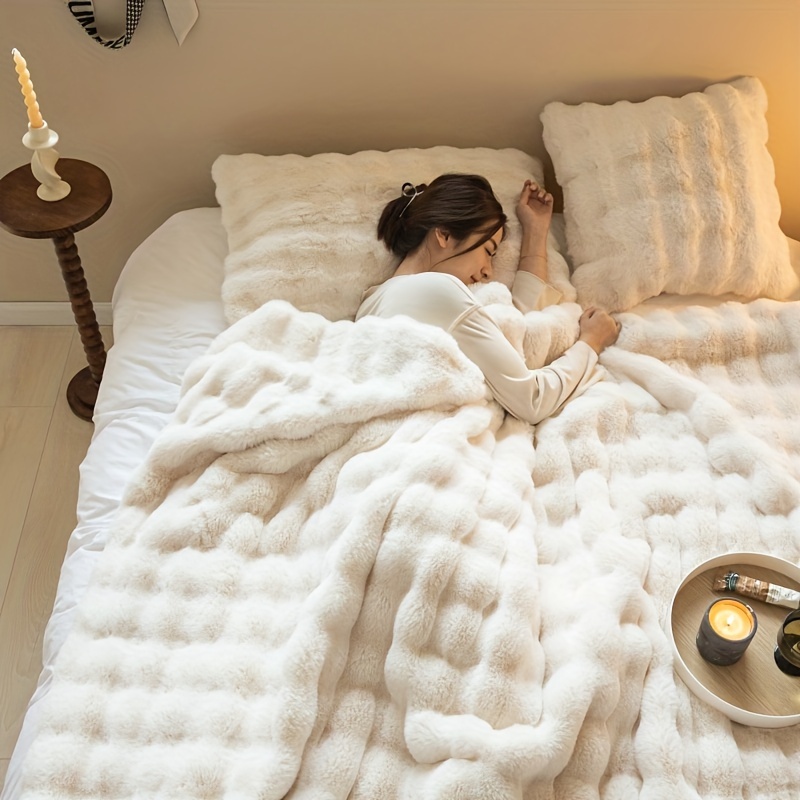 Person sleeping under a fluffy blanket on a bed, with a side table and candle nearby.