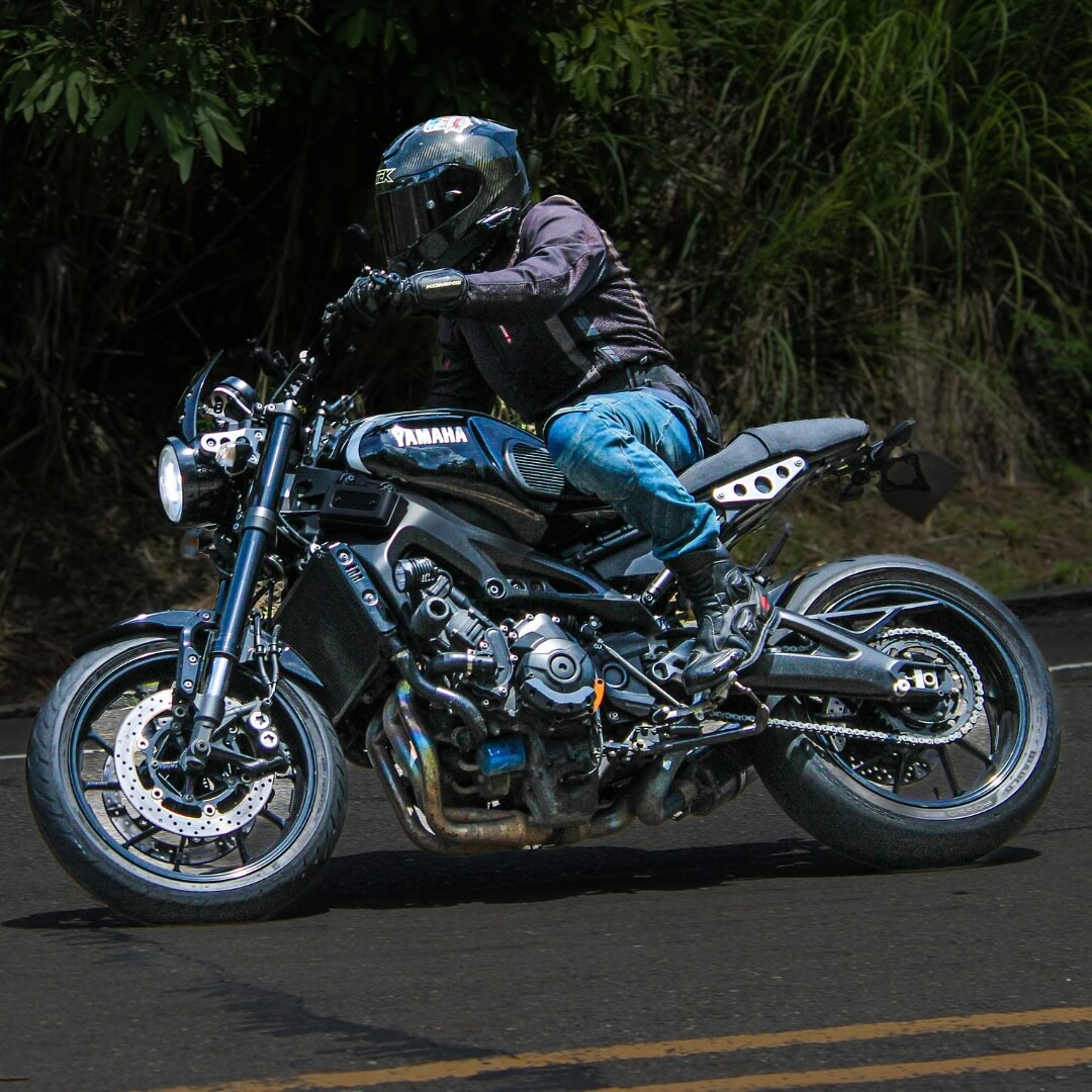 Motorcyclist in protective gear riding a Yamaha on a road with greenery.