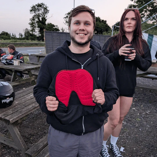 Two people outdoors, one holding a red object, another with a drink.