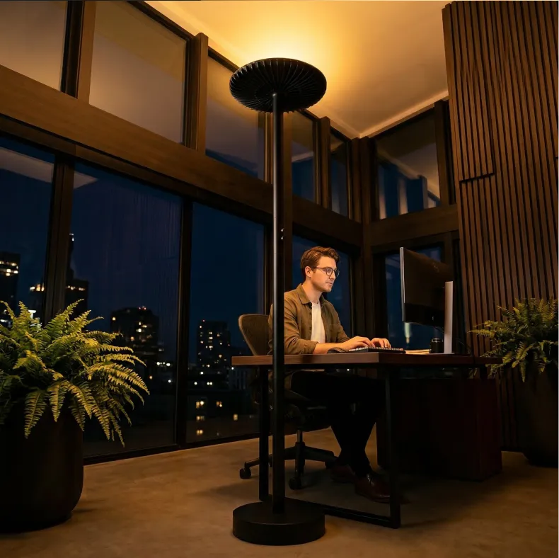 A man works at a desk in a modern, warmly lit office at night with a city view.