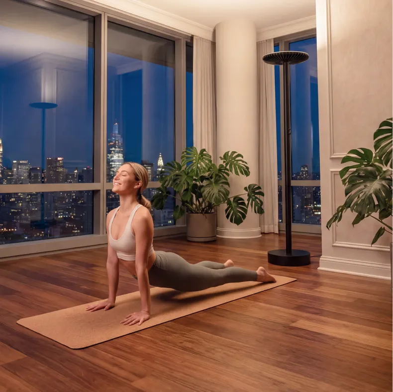 A woman does yoga on a mat in an apartment overlooking a city skyline at night.