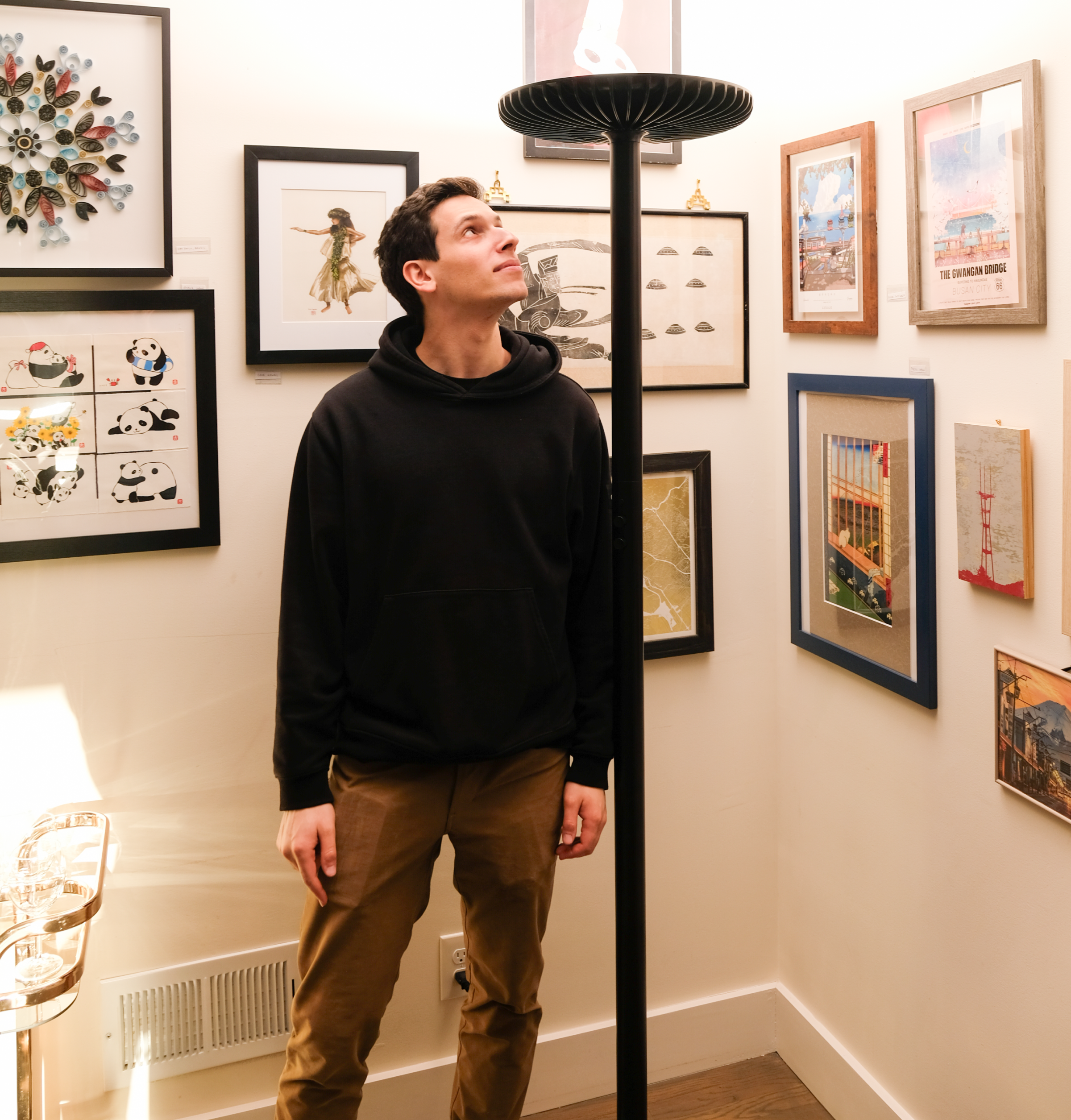A person standing beside a black Brighter floor lamp in a room with framed artwork.