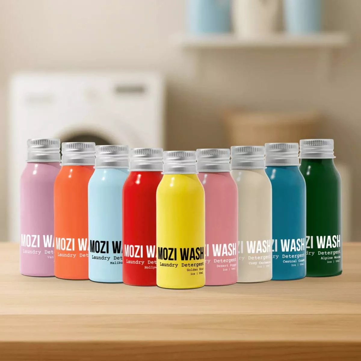 A row of nine small, colorful bottles of Mozi Wash laundry detergent on a wooden surface.