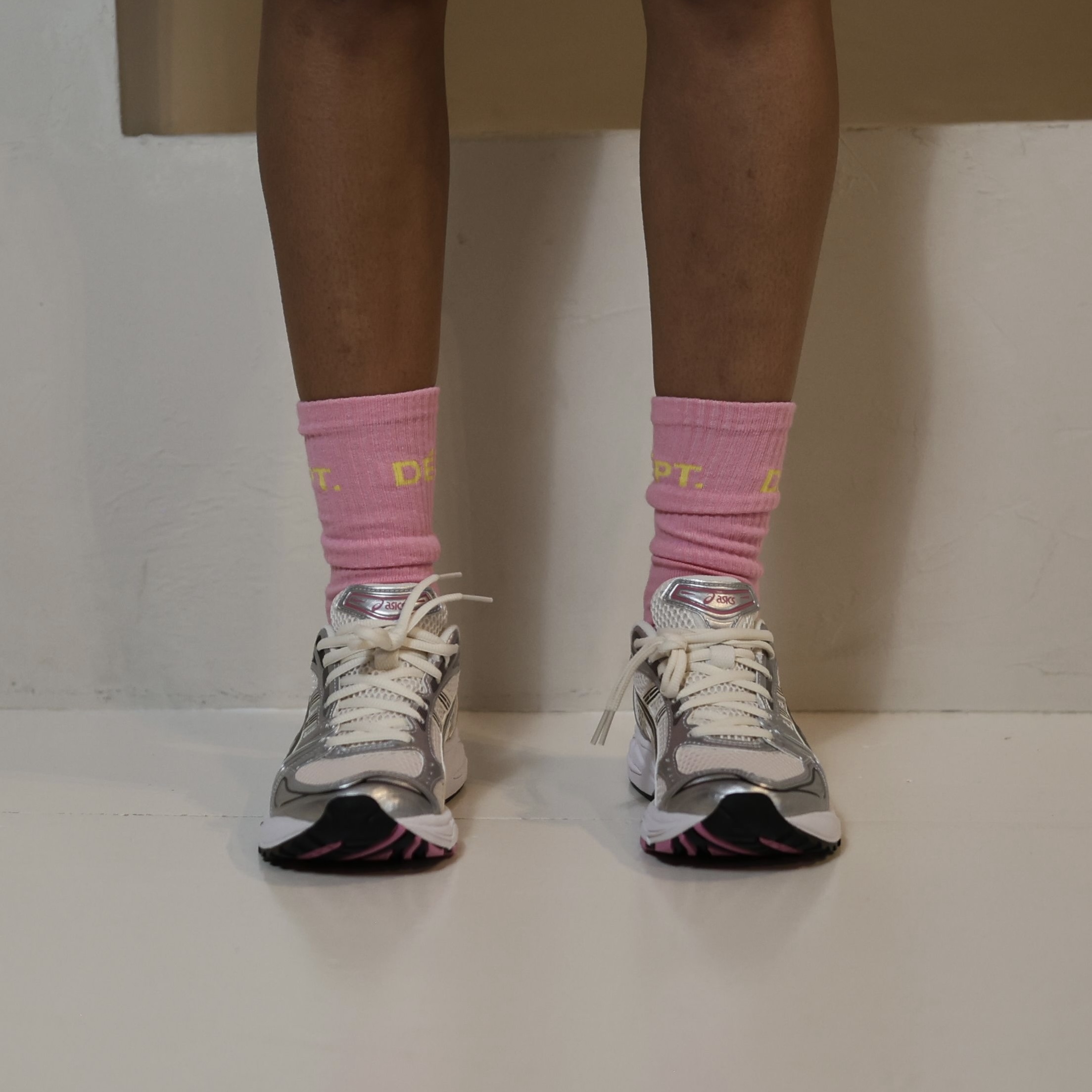 Person wearing pink socks and silver sneakers on a white surface.