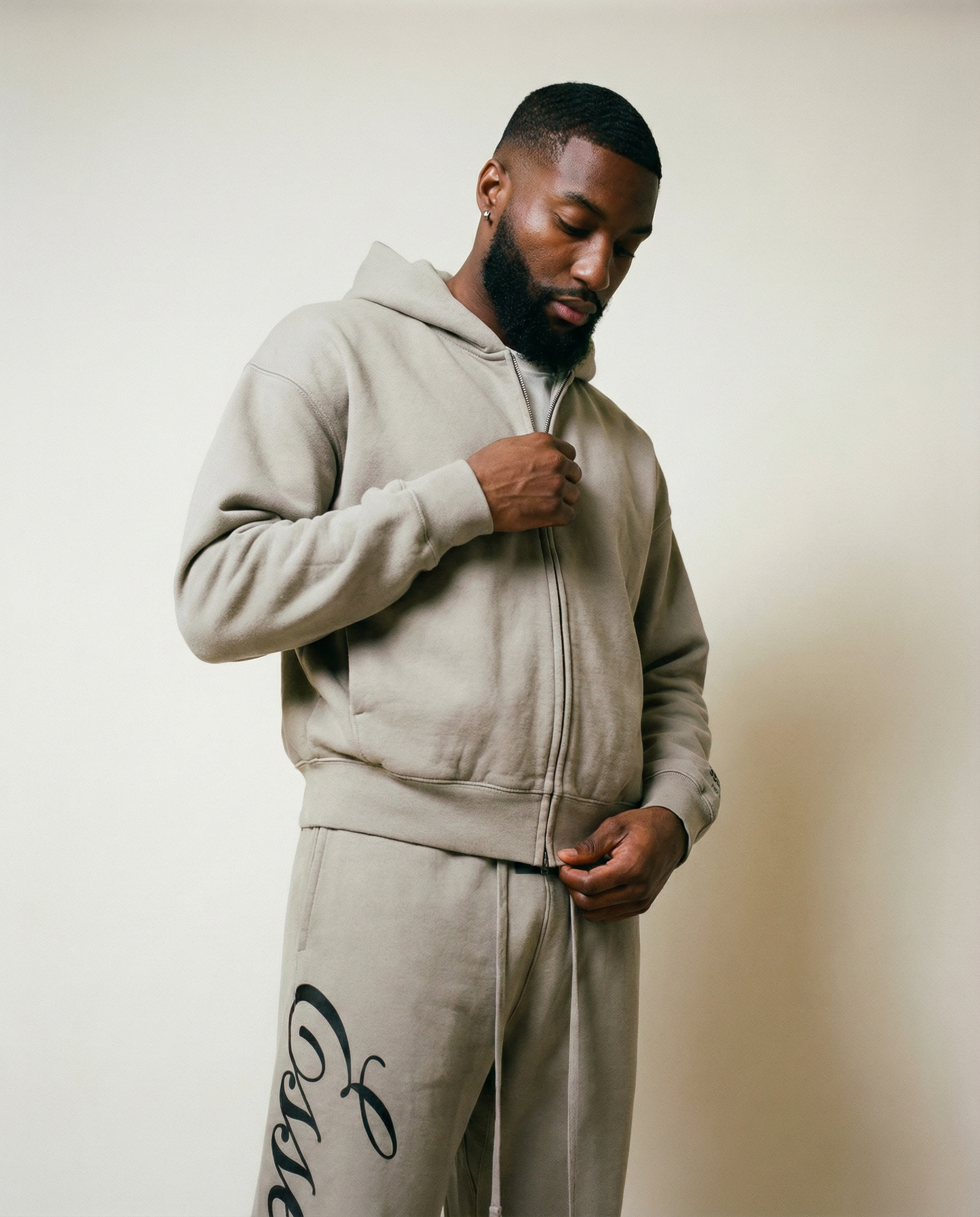 A man in a gray zip-up hoodie and matching sweatpants looks down as he zips it.