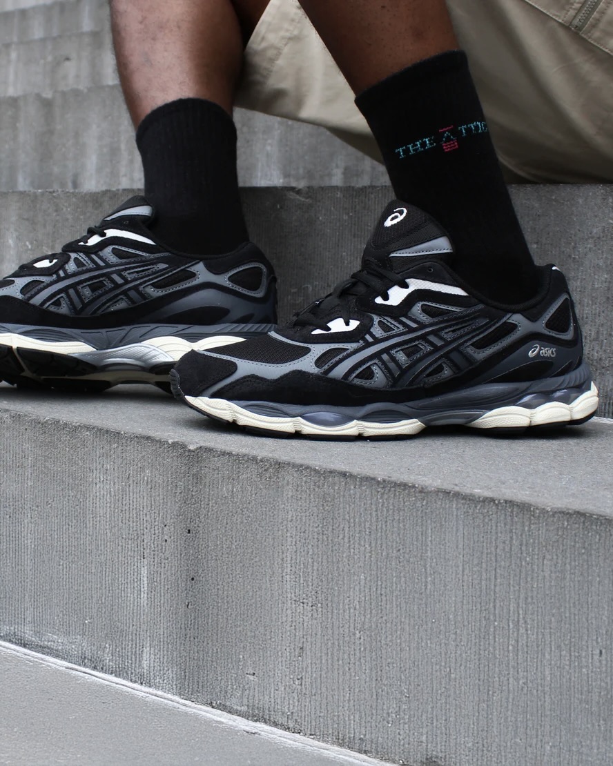 A person wearing black and grey Asics sneakers and black socks on concrete steps.