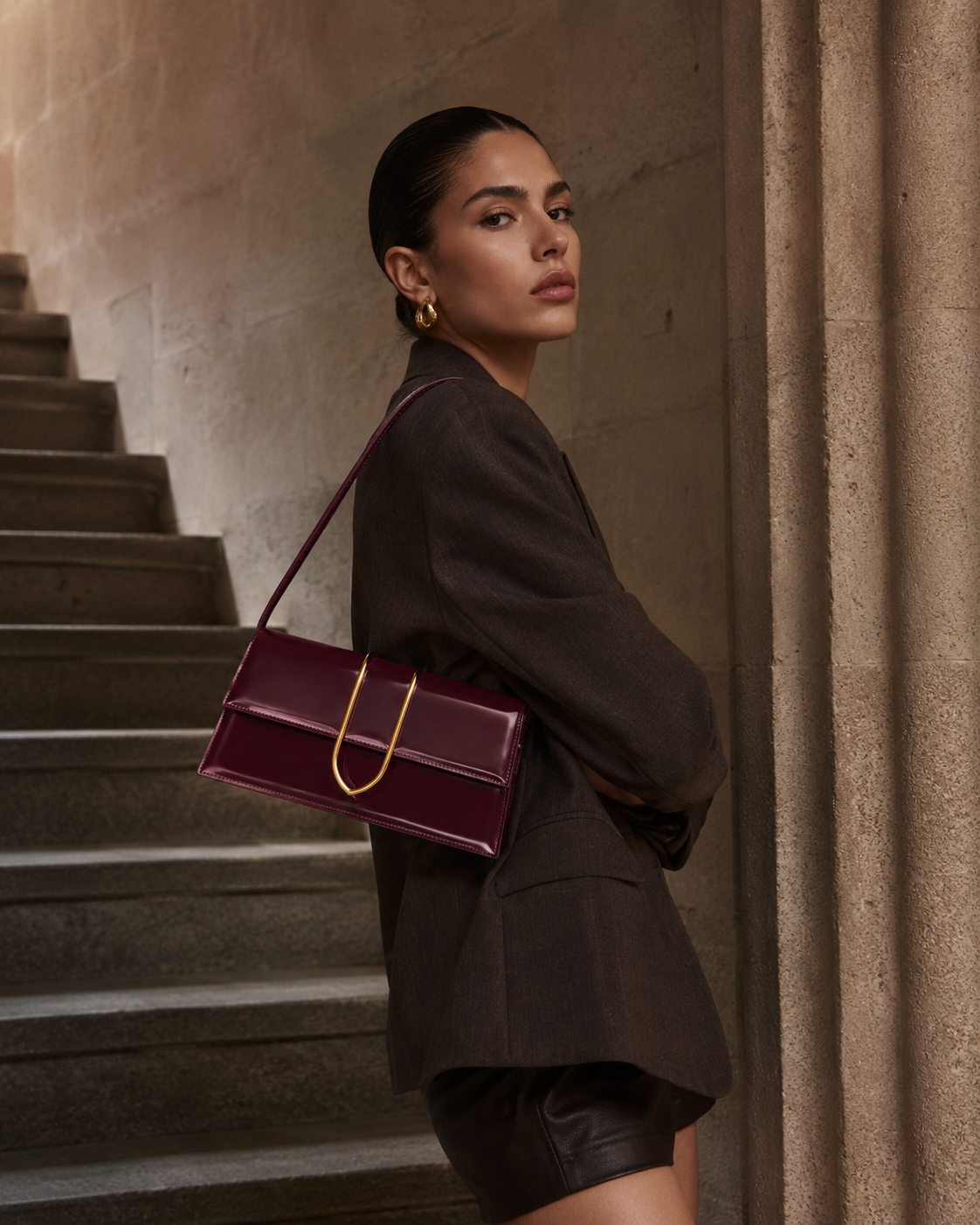 A woman in a dark blazer looks over her shoulder, holding a burgundy handbag on a staircase.