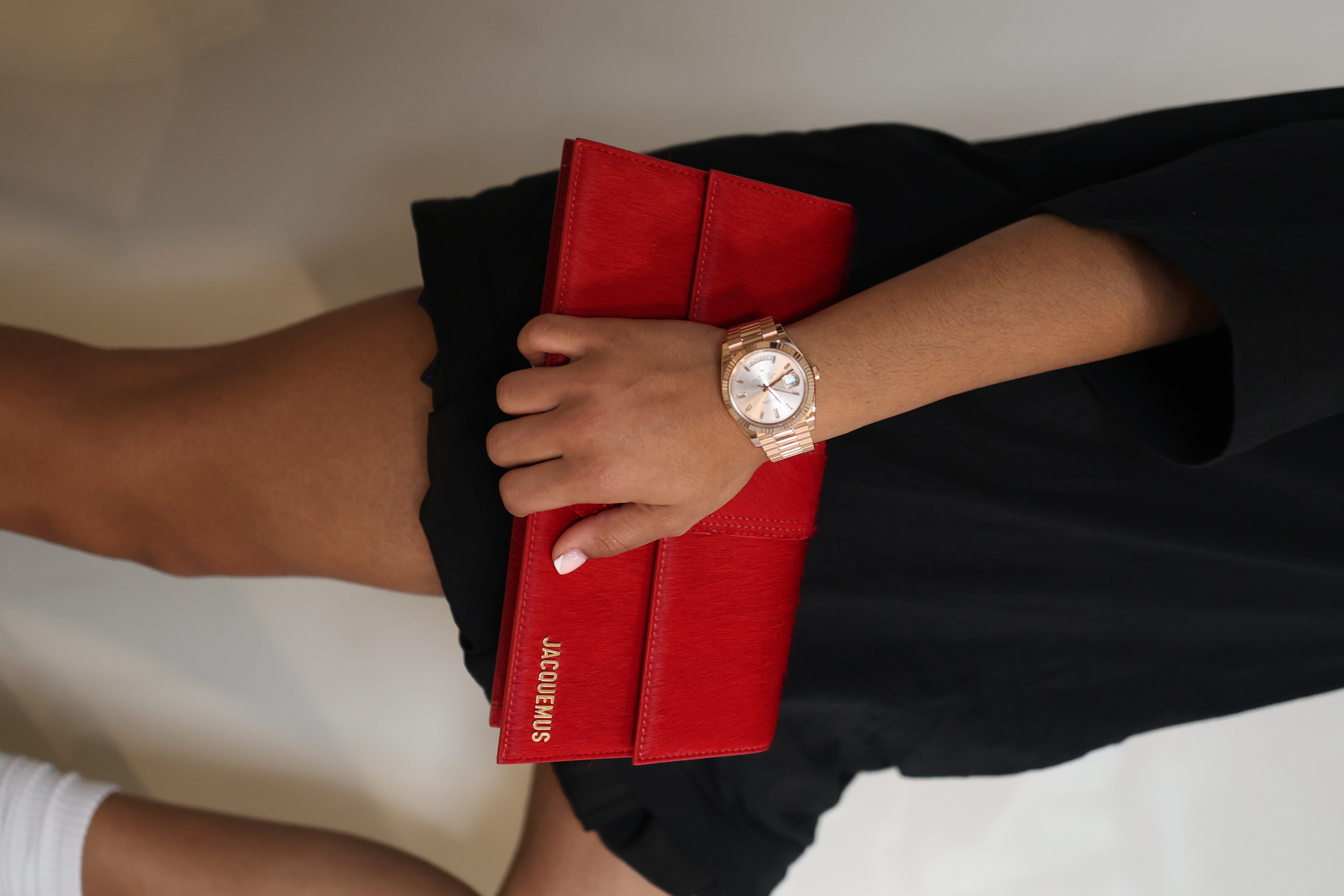 Person holding red Jacquemus clutch and wearing a watch.