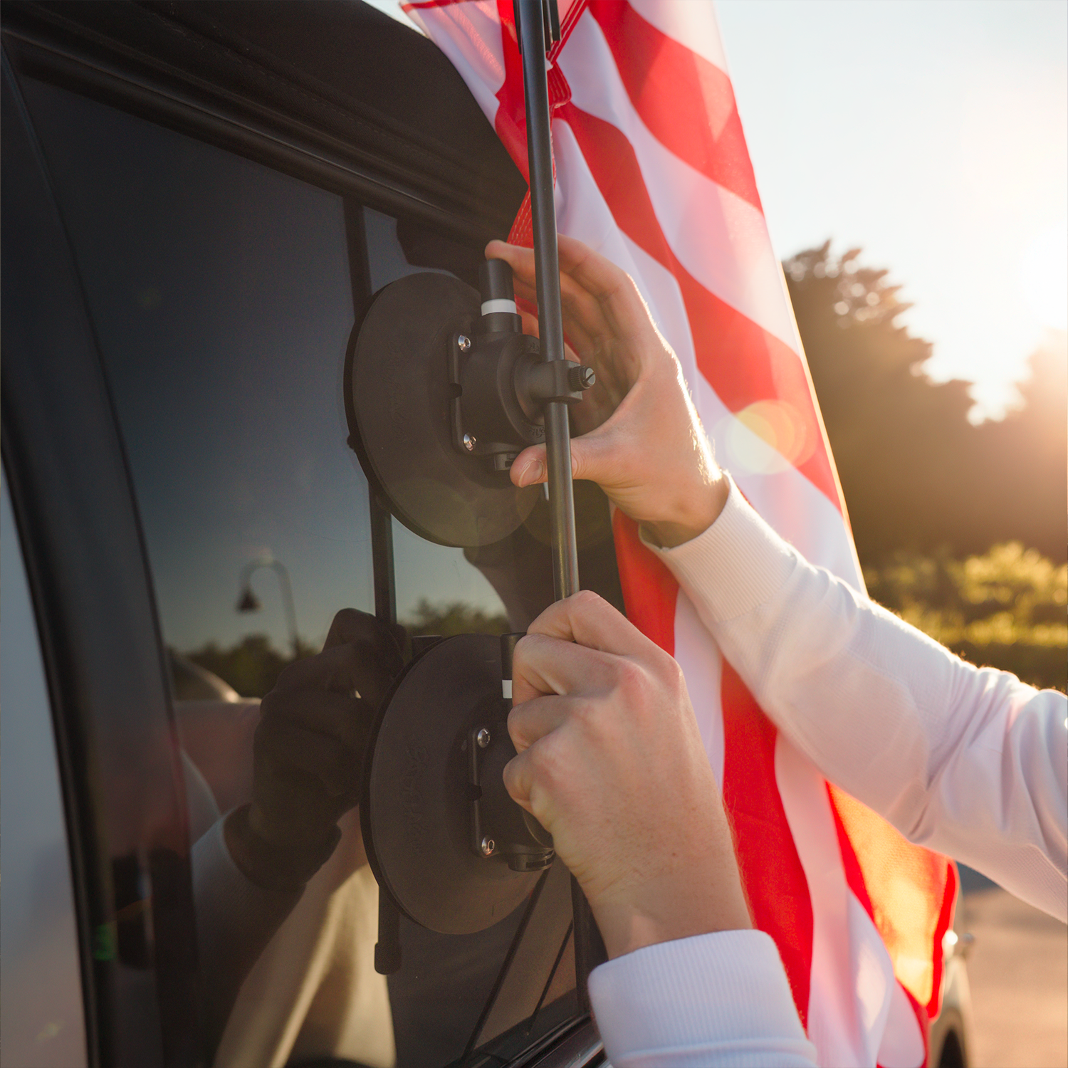 A person attaching an American flag to a car window with a suction cup mount at sunset.