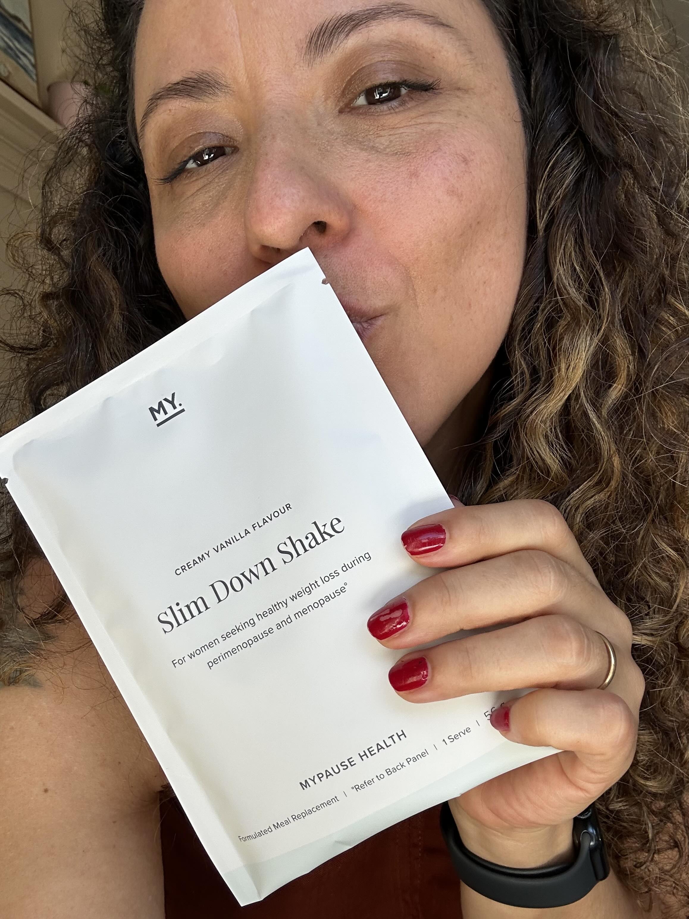 Person holding a white packet labeled 'Slim Down Shake' with red-painted nails.