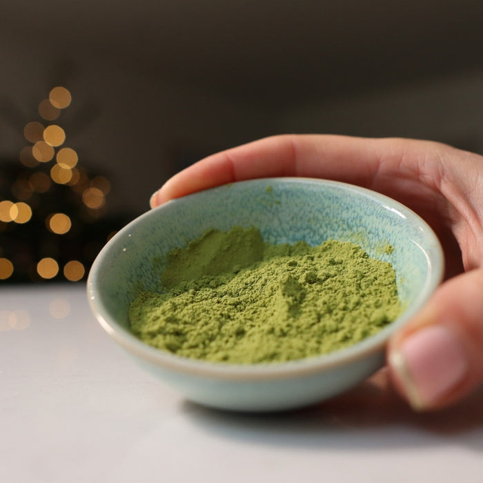 A hand holding a small bowl of green powder.