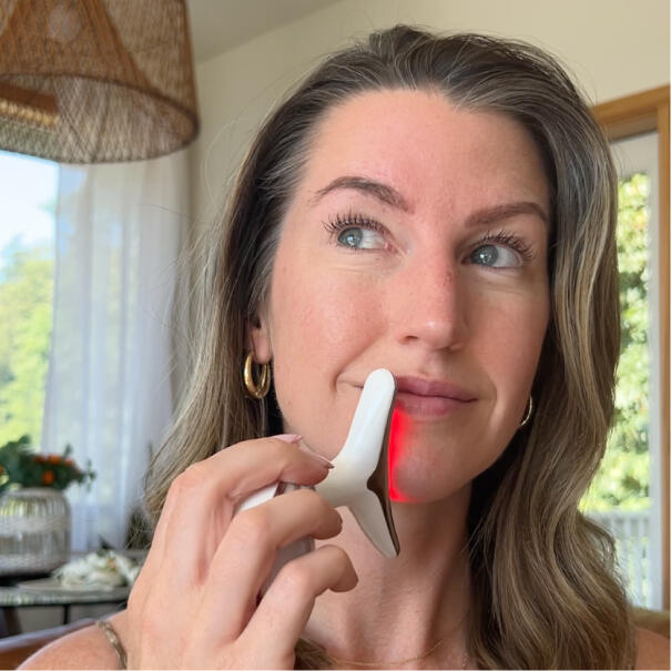 Person using a skincare device with a red light on their face.