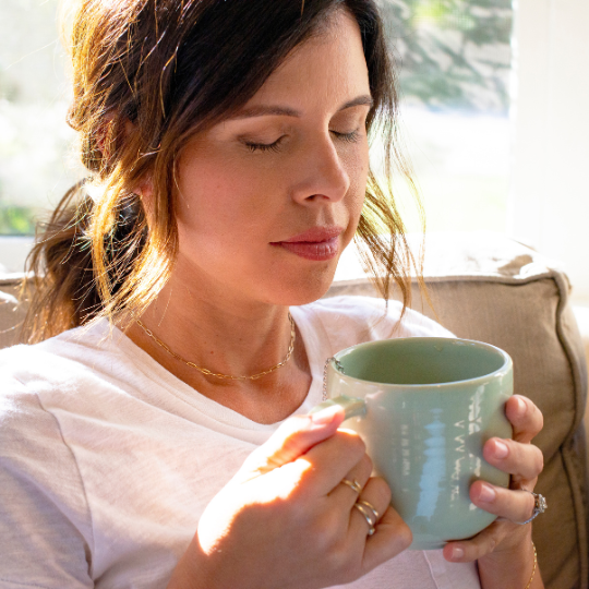 Person holding a large green mug, sitting indoors with eyes closed.